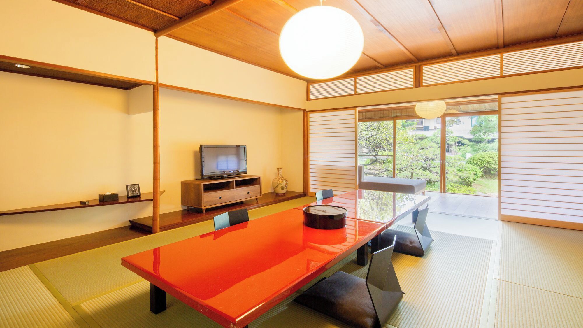 Ein traditioneller japanischer Raum mit Tatami-Boden, einem niedrigen Tisch, einem Fernseher und Blick ins Grüne.