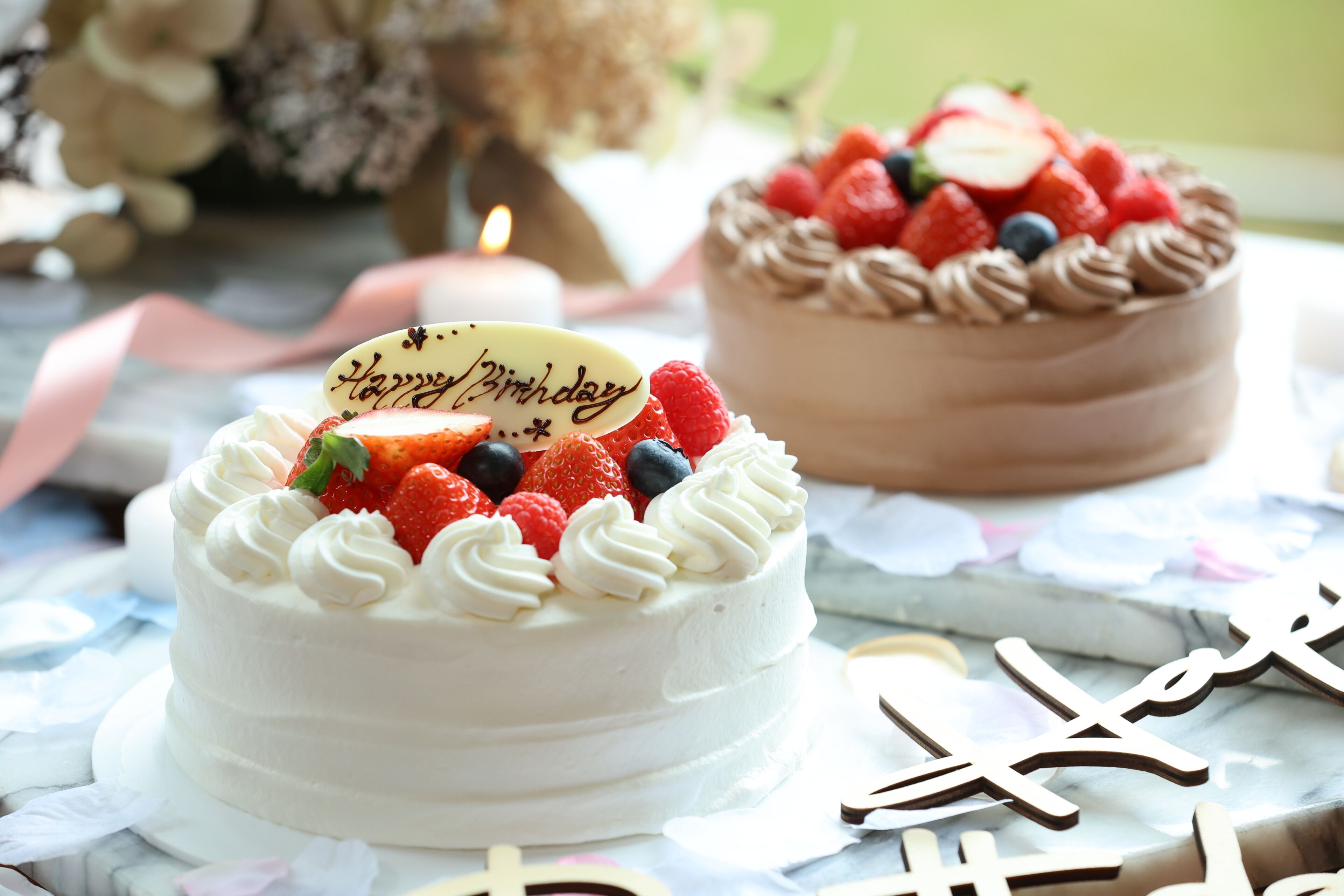 Deux gâteaux décorés avec l’inscription « Joyeux anniversaire » sont posés sur une table à motifs floraux.