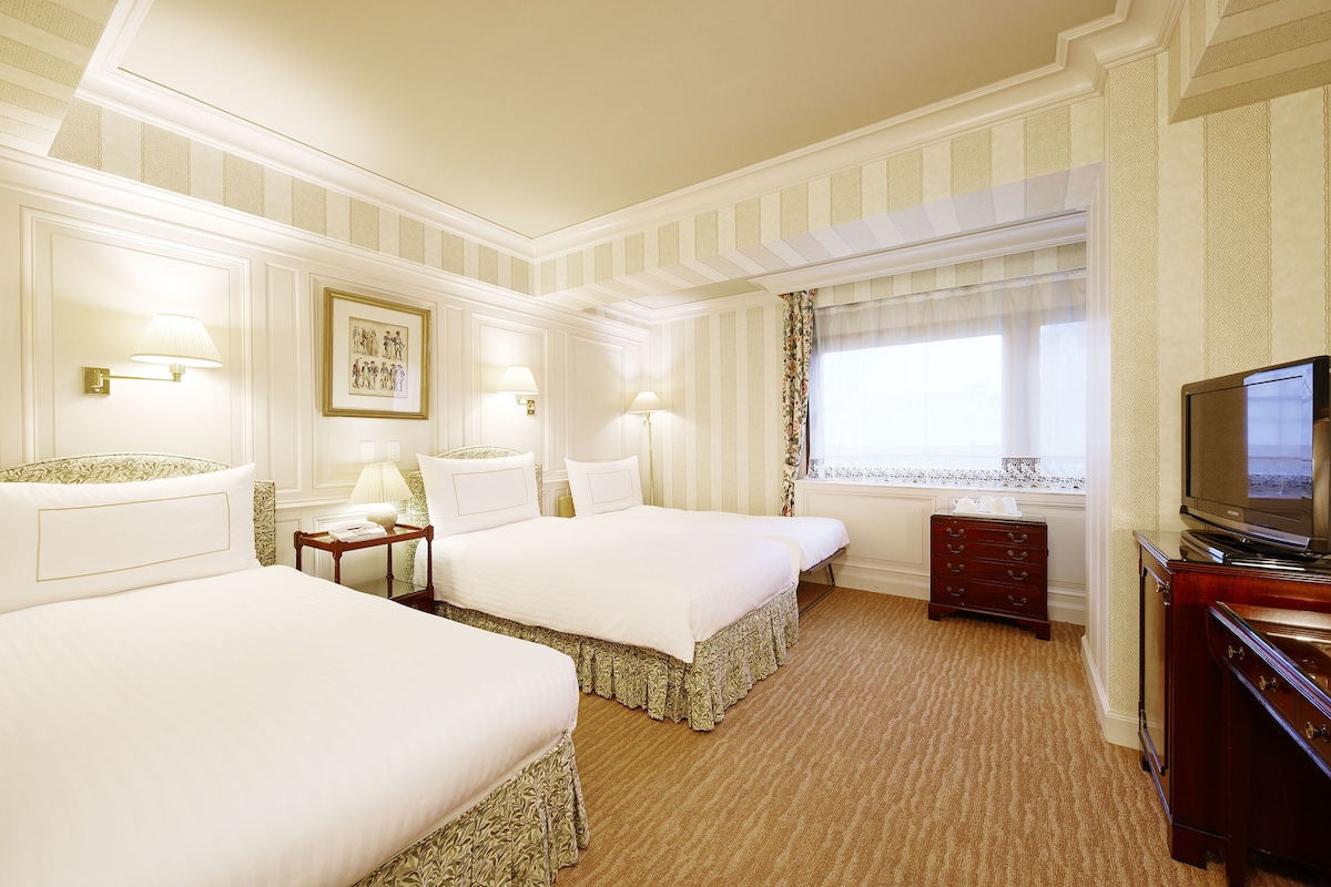 Habitación de hotel con dos camas, televisión, cómoda y ventana con cortinas.