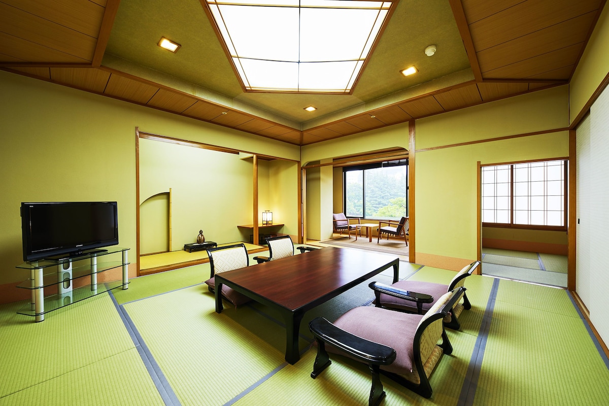 Una habitación tradicional japonesa con suelo de tatami, una mesa baja de tatami y un televisor sobre un pedestal.