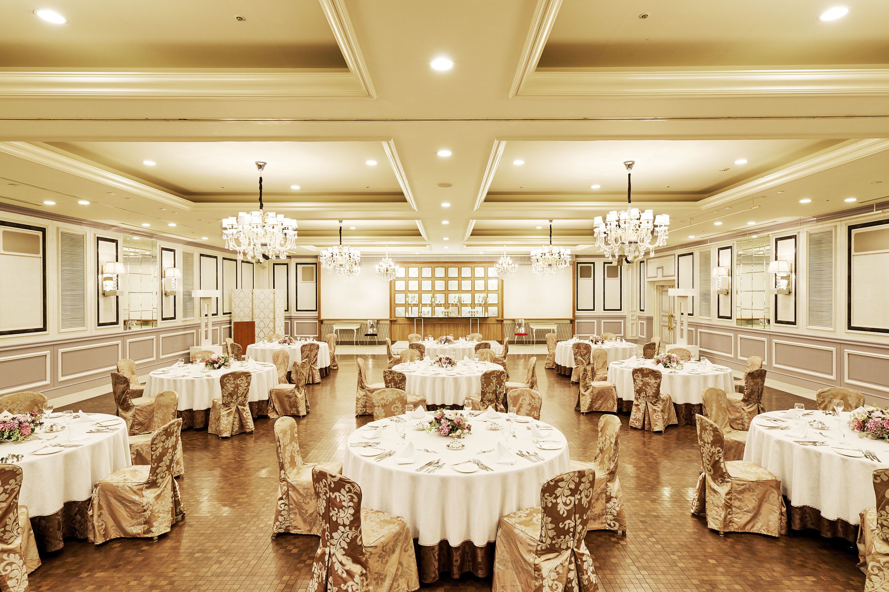 Une salle de banquet avec des tables rondes et des chaises, des lustres et des tableaux encadrés aux murs.