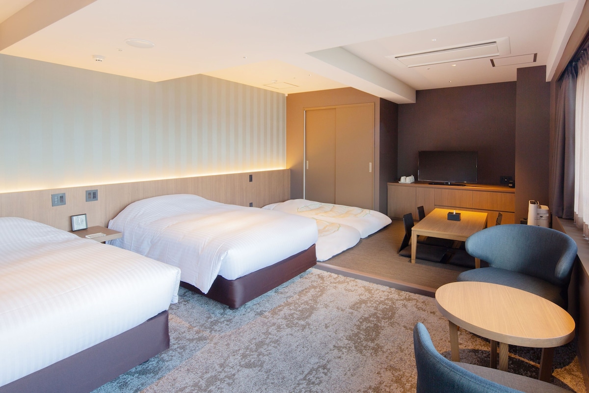 Habitación de hotel con dos camas, un escritorio, una silla, un televisor y un minibar.