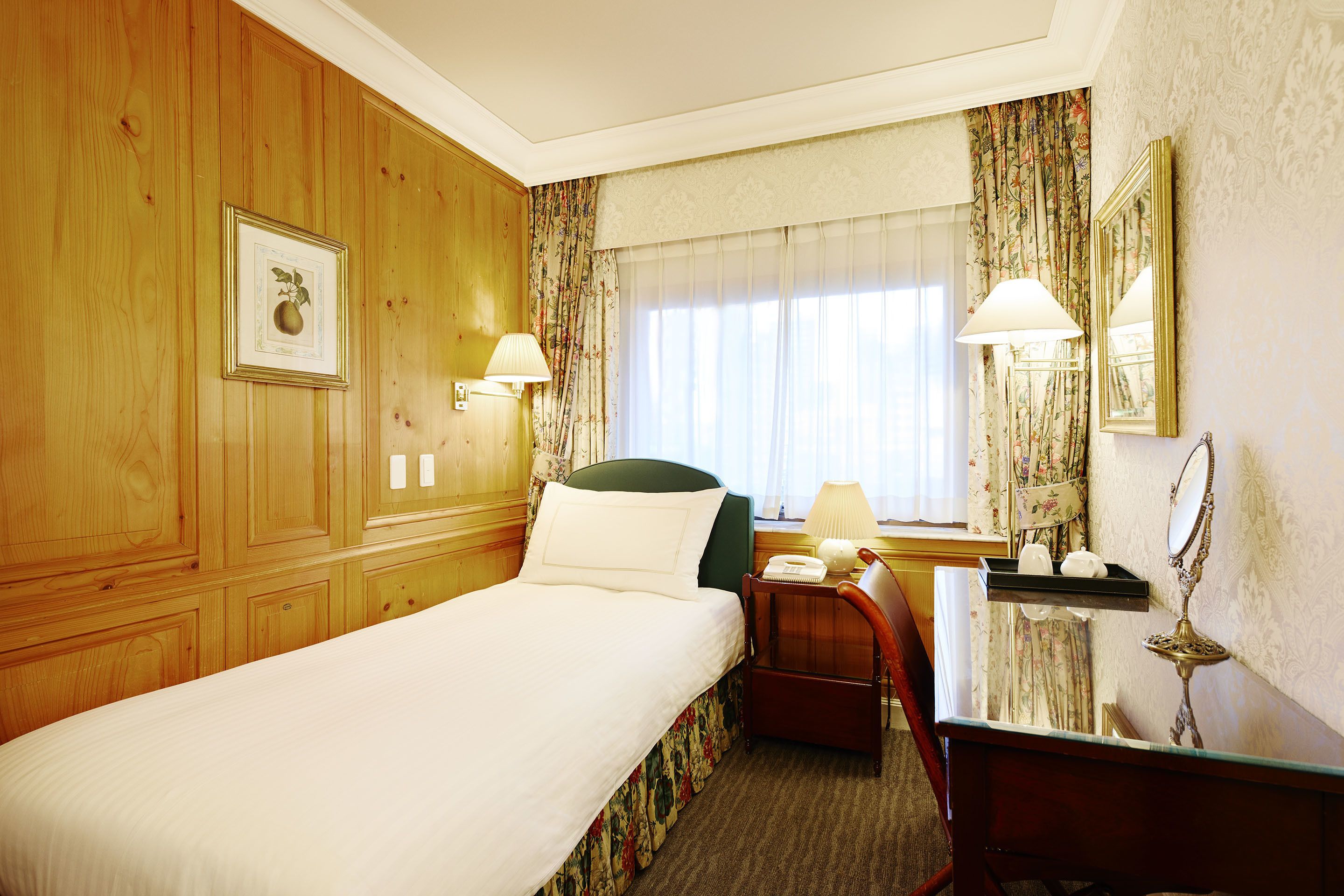 Une chambre d’hôtel avec un grand lit, un bureau, une chaise, une table de chevet, une lampe, un miroir et une fenêtre avec des rideaux.