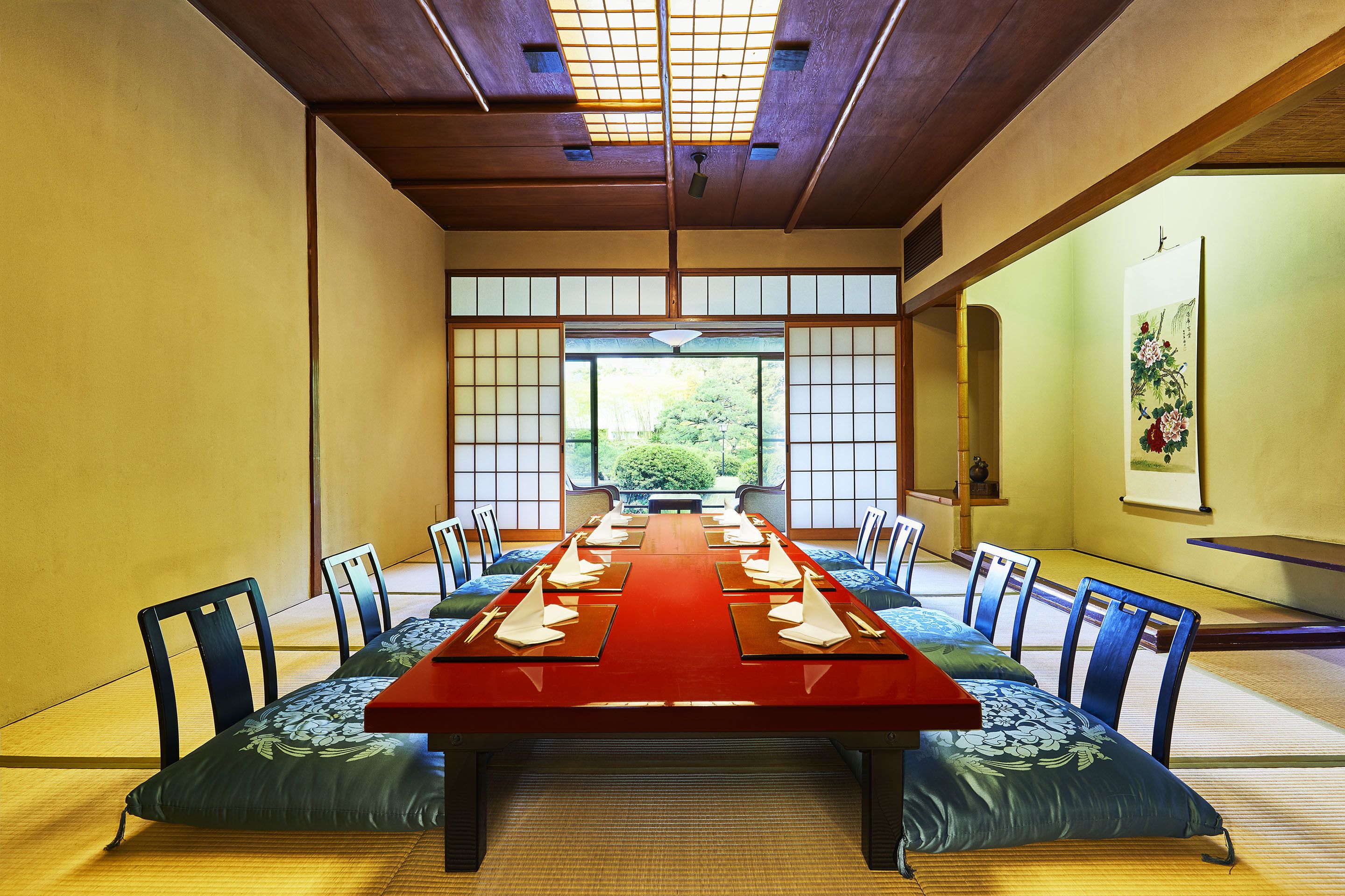 A traditional Japanese-style meeting room with tatami mats, a long wooden table, and low wooden chairs.