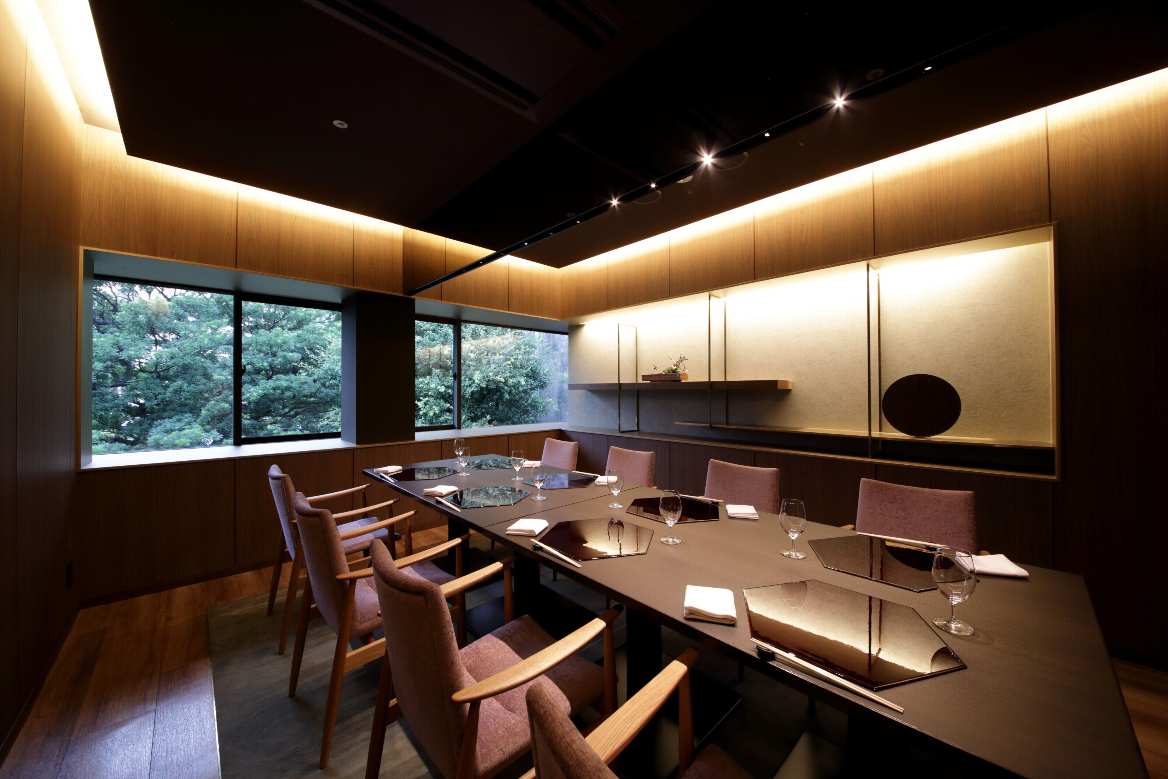 A conference room with a long table, chairs, and a view of trees through large windows.