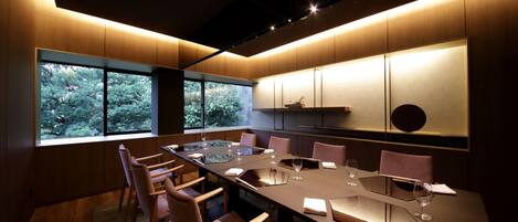 A conference room with a long table, chairs, and a view of trees through large windows.