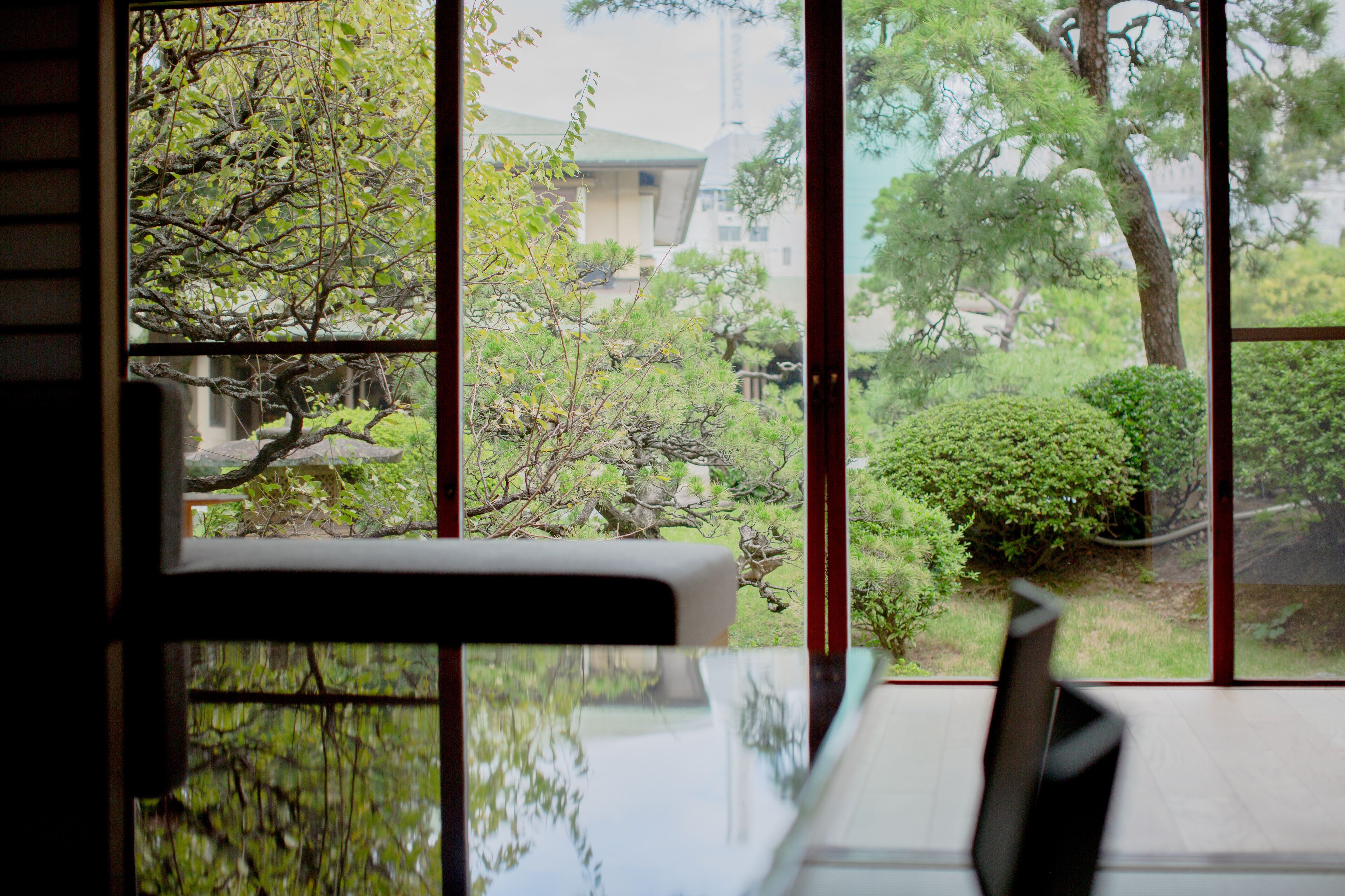 A room with a large window offering a view of a garden with trees and a building in the background.