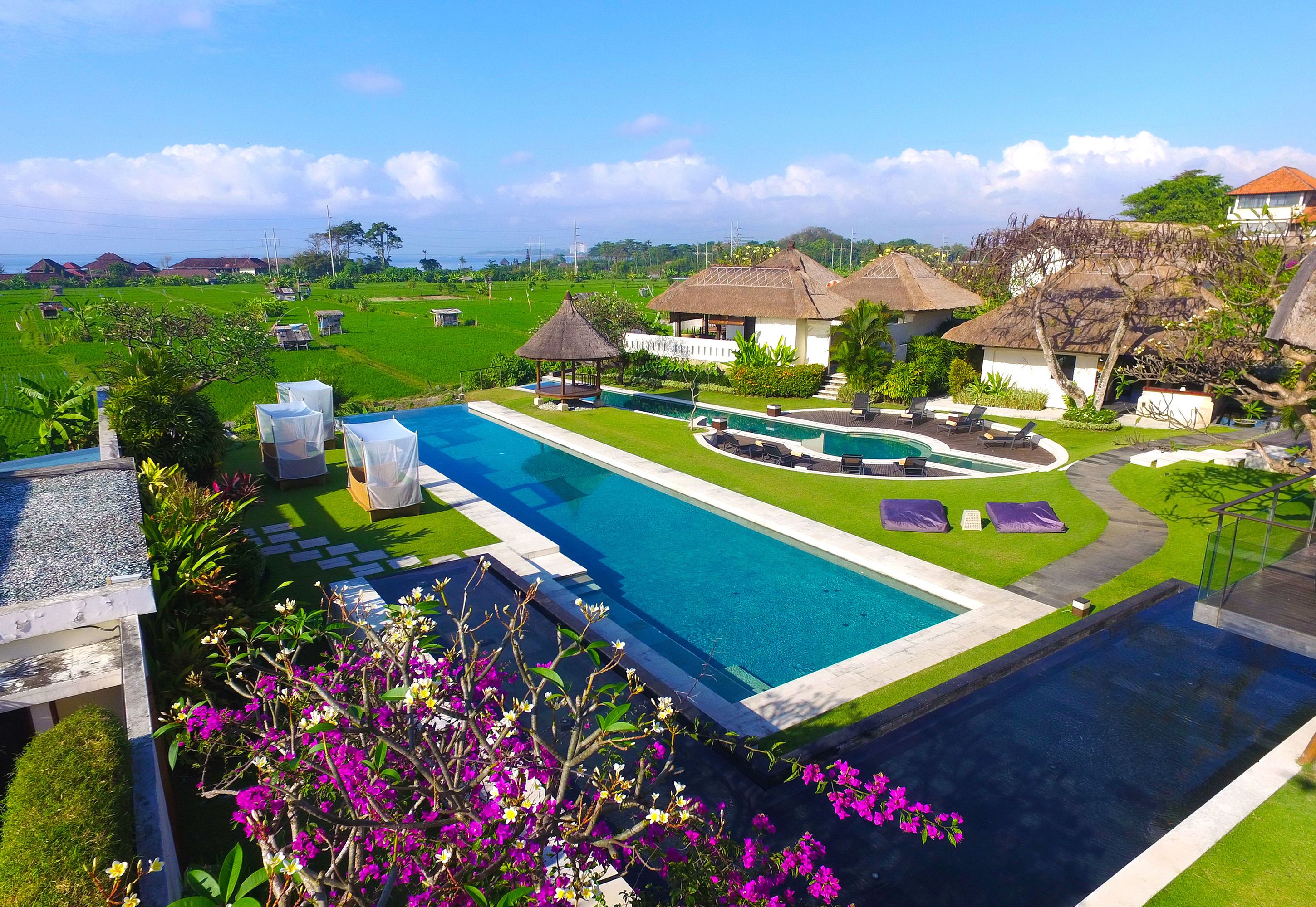 Un resort con una amplia piscina, cabañas de techo de paja y exuberante vegetación.