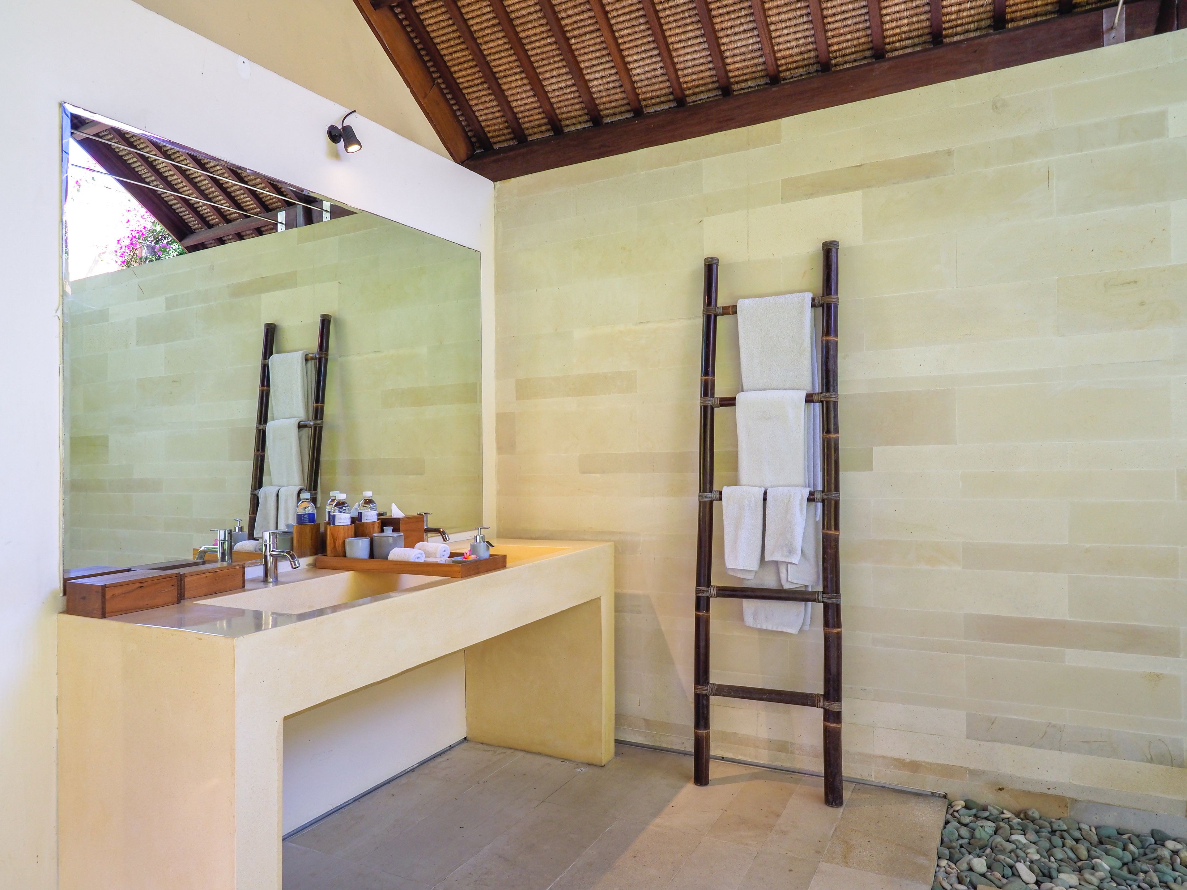 Un baño con un espejo grande, una escalera de madera con toallas, un tocador color beige y una pared con azulejos.