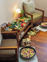 A room with a wooden table set with various items, including a bowl of flowers, a lamp, and a potted plant.