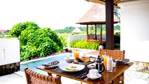 Une table de salle à manger dressée pour le petit-déjeuner, avec vue sur une piscine et une végétation luxuriante.