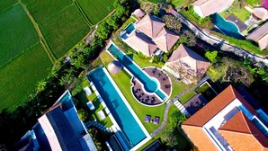 Vue aérienne d’un complexe hôtelier doté d’une piscine, de plusieurs bâtiments et entouré de champs verdoyants.