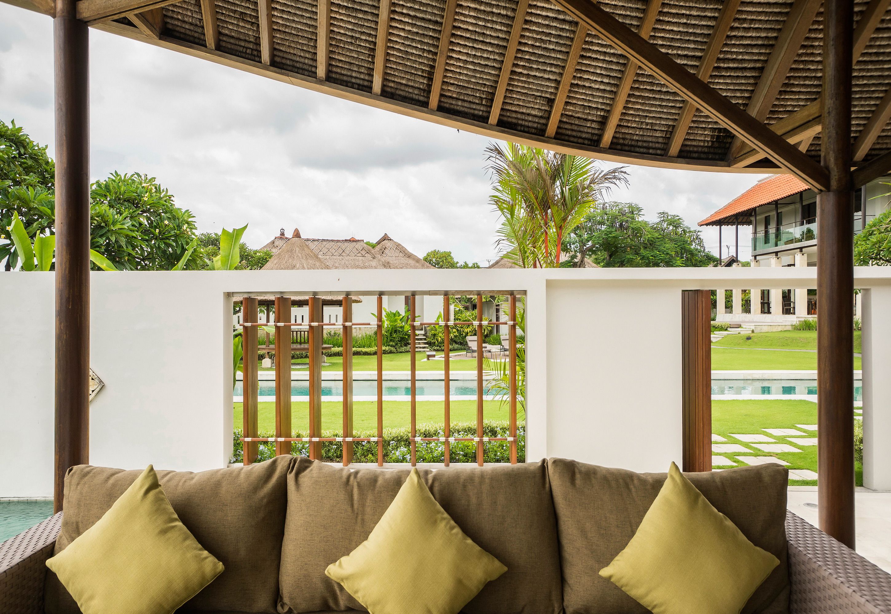 Un espacio de estar al aire libre cubierto con vistas a una piscina y un jardín bien cuidado.