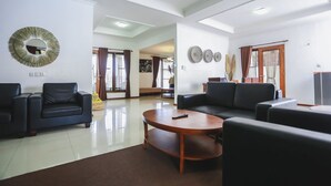 A spacious living room with two black sofas, a wooden coffee table, and a large mirror on the wall. - Kuldesak Villas (Bandung)