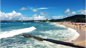 A beach with waves, a sandy shore, and a distant view of buildings and hills. - Warehouse Inn (Hengchun)