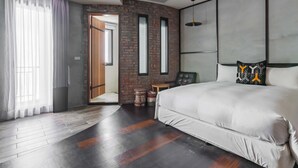 A modern hotel room with a large bed, a wooden floor, a brick accent wall, and a view of the outside. - Warehouse Inn (Hengchun)