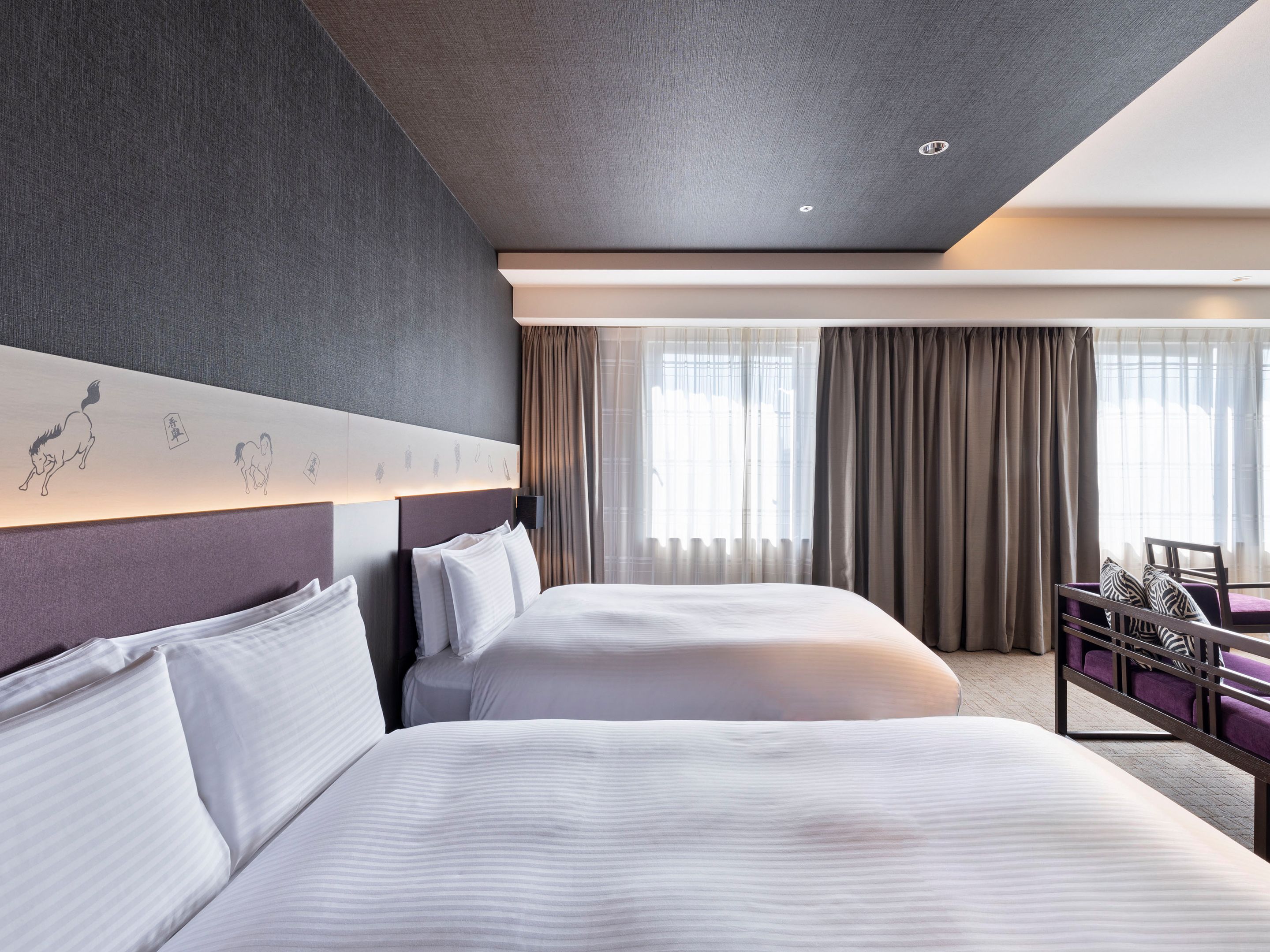 A hotel room with two beds, a headboard with artwork, a desk with a chair, and a large window with curtains.