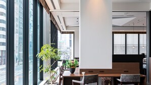 A modern dining area with a wooden table, two chairs, a potted plant, and a view of the city through large windows. - Mitsui Garden Hotel Kyobashi Tokyo Station (Tokyo)