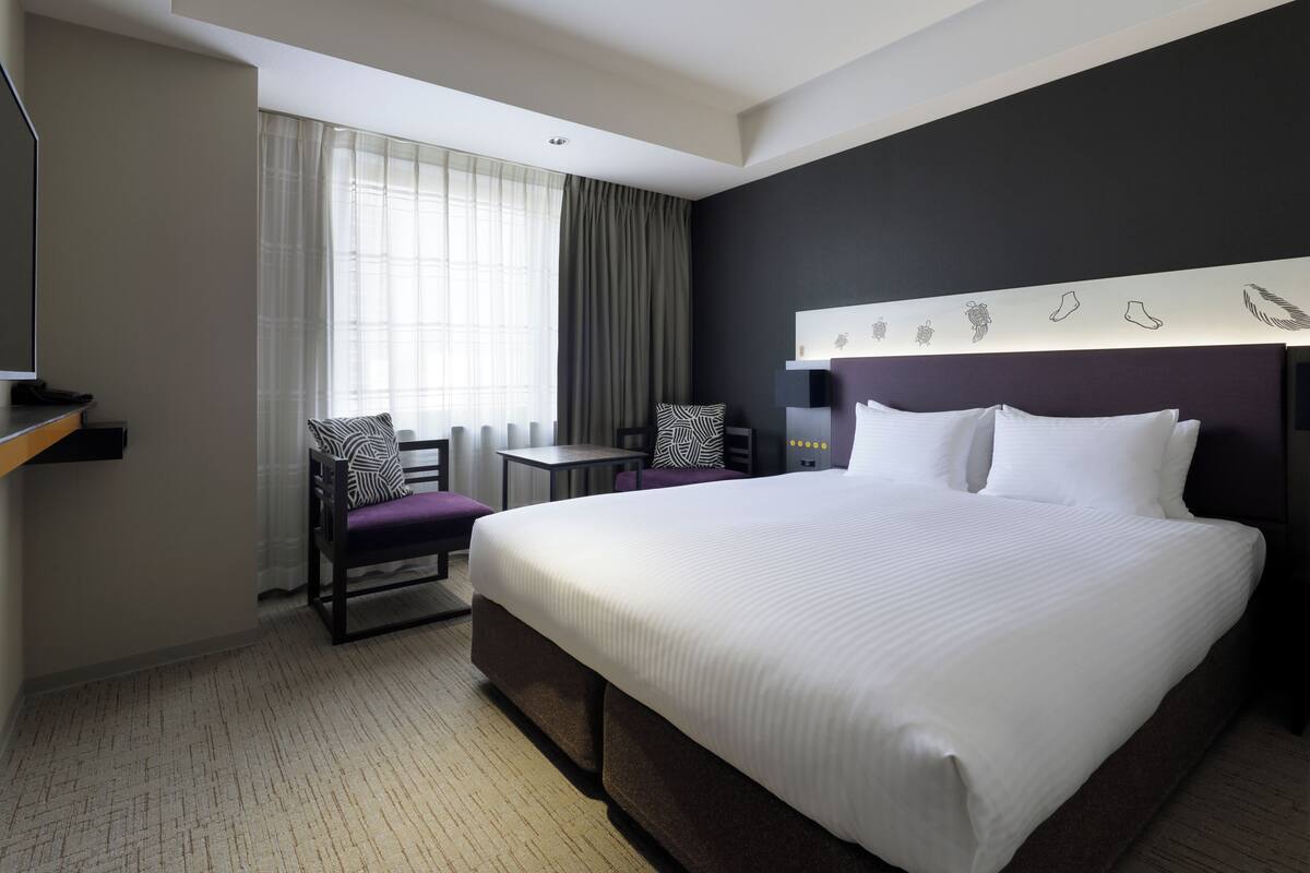 Una habitación de hotel con una cama grande, un escritorio, una silla y un televisor.