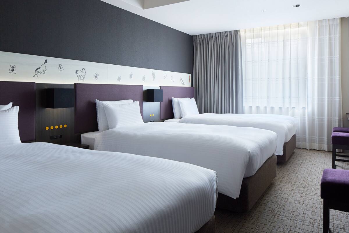 Habitación de hotel con dos camas, cabecero decorado con una obra de arte, escritorio y ventana con cortinas.