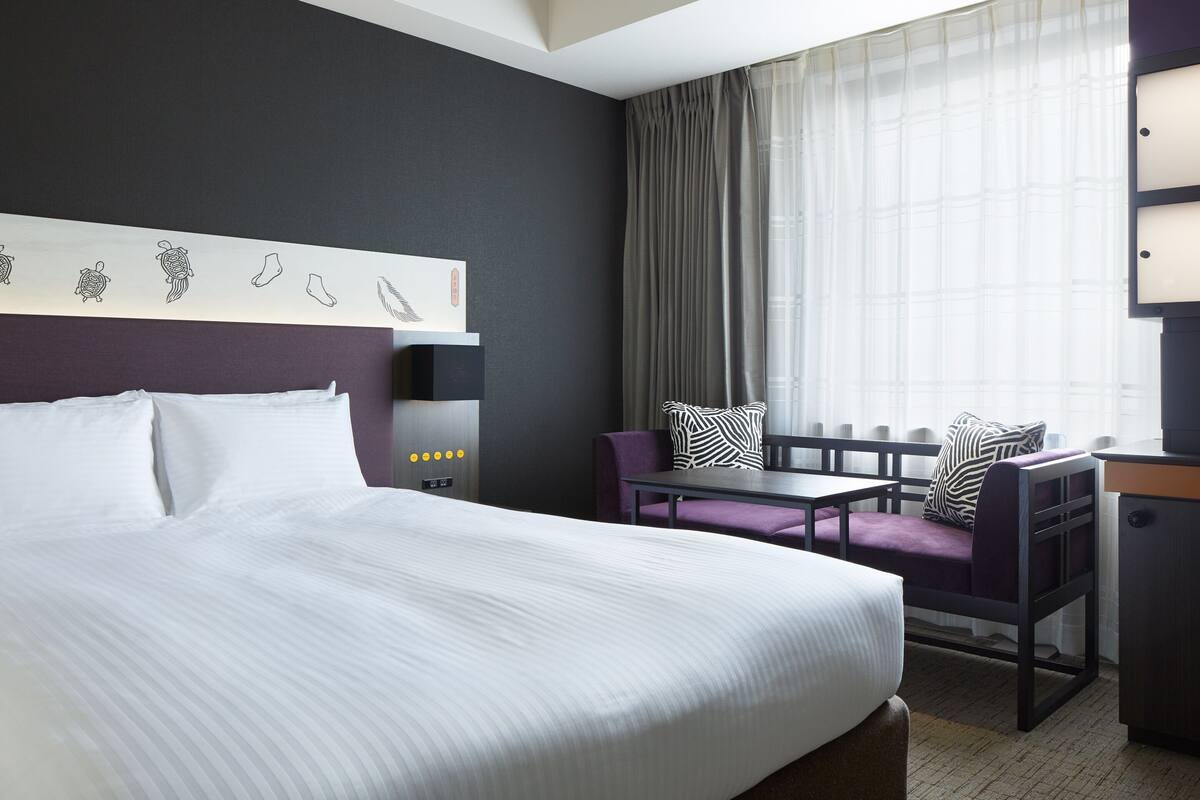 Una habitación de hotel con una cama grande, un escritorio, una silla y una ventana con cortinas.