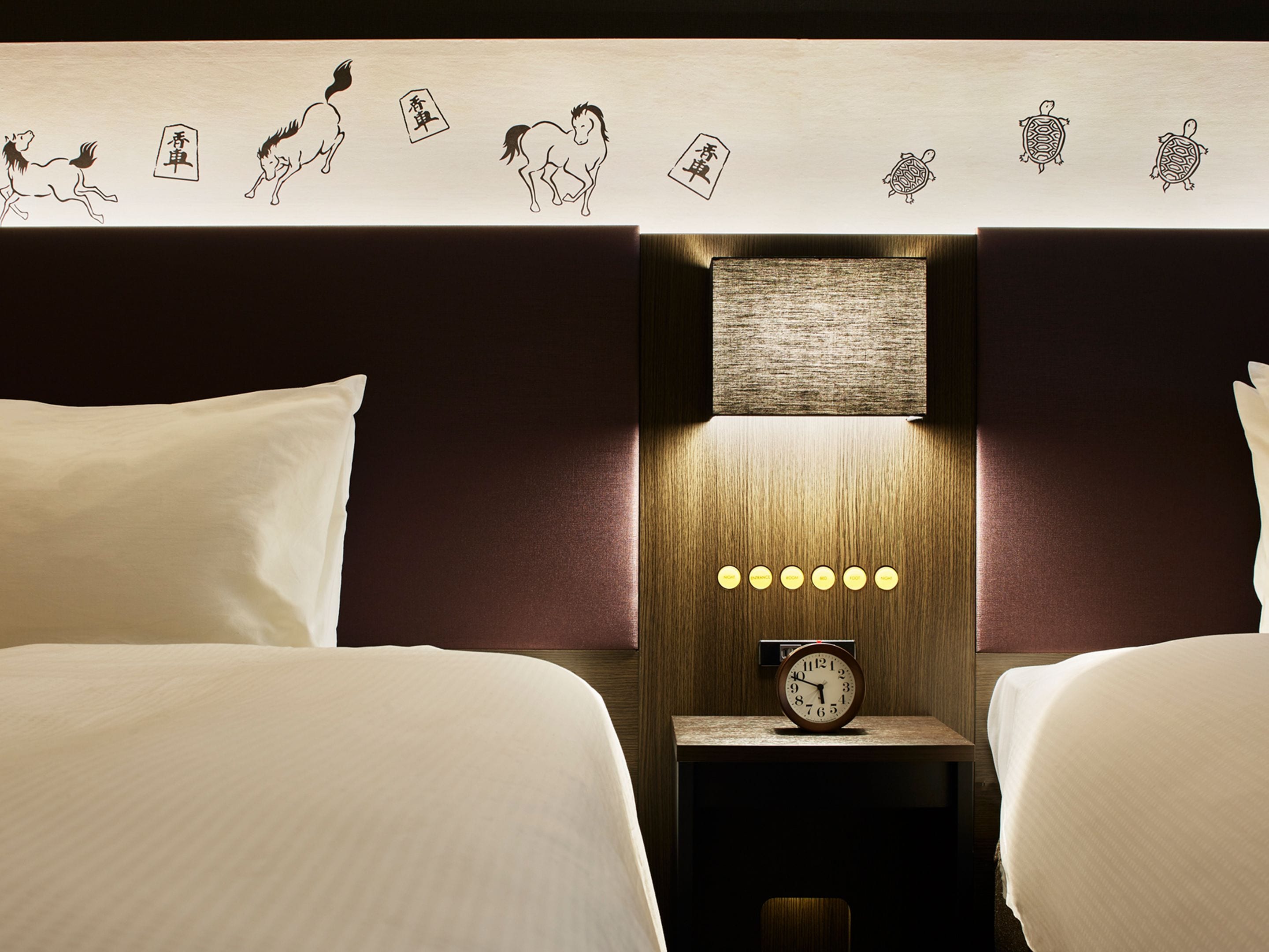 A hotel room with two beds, a nightstand with a clock, and decorative wall art featuring animals.