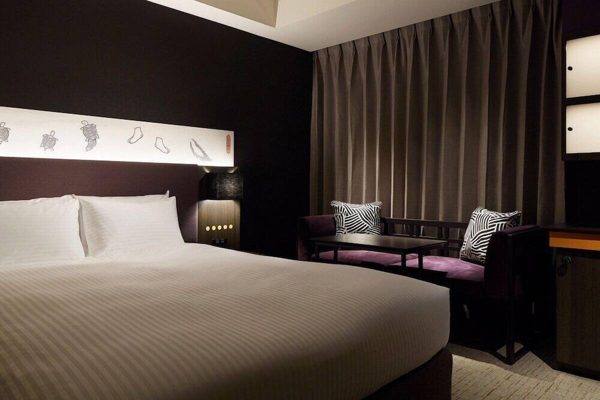 Una habitación de hotel con una cama grande, un escritorio, una silla y una cortina.