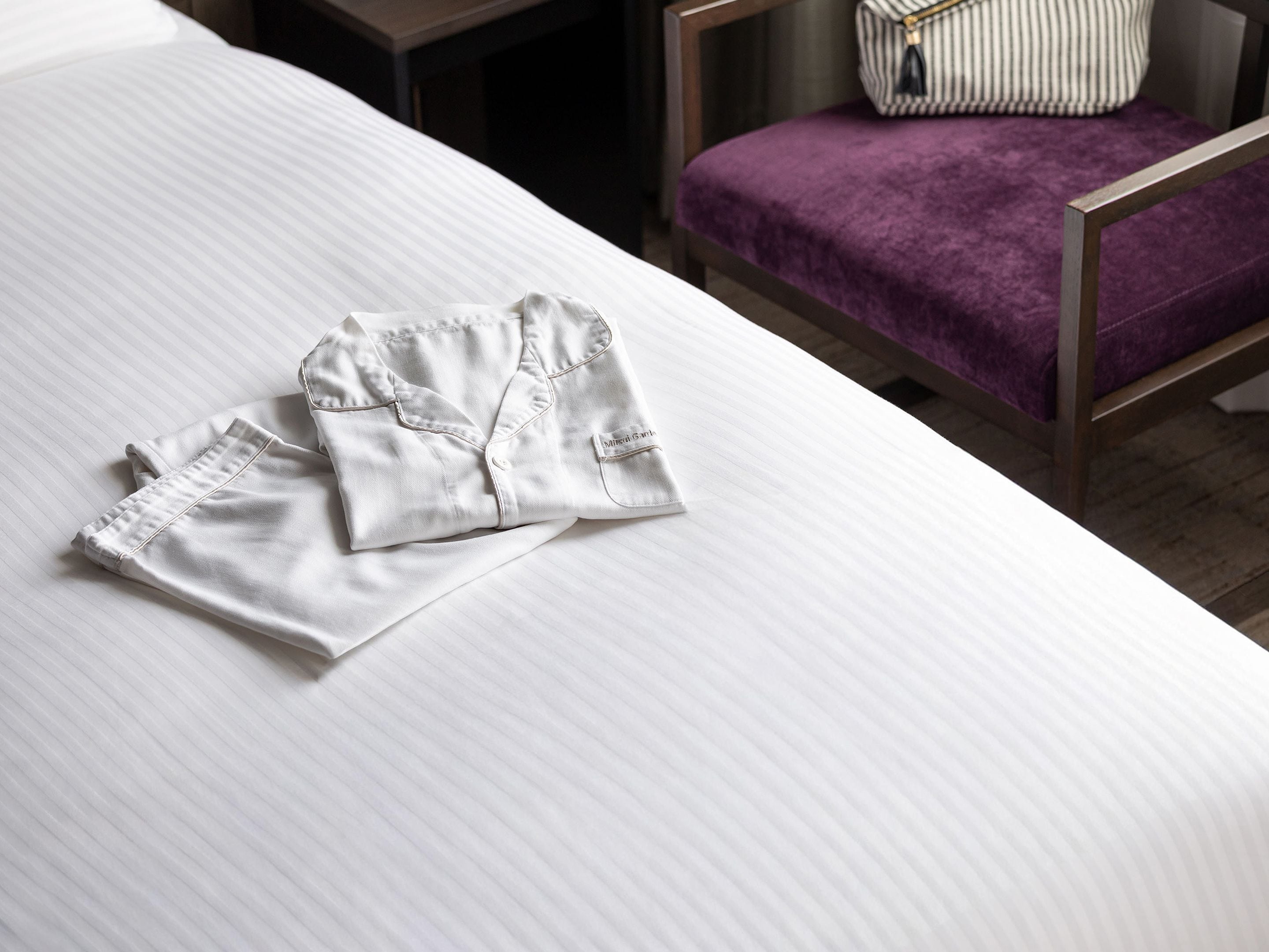Una cama bien hecha con un almohadón a rayas y un cojín morado sobre una silla de madera.