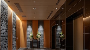 Un moderno vestíbulo de ascensor con piso a cuadros, paneles de madera y piedra, y plantas en macetas.