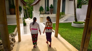Two women walking on a paved pathway towards a building with a white exterior and columns. - Villa Greenday (Cepaka)