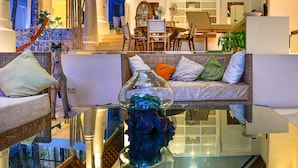 A modern living room with a glass coffee table, wicker furniture, and a dining area with wooden chairs and a white table. - Villa Greenday (Cepaka)
