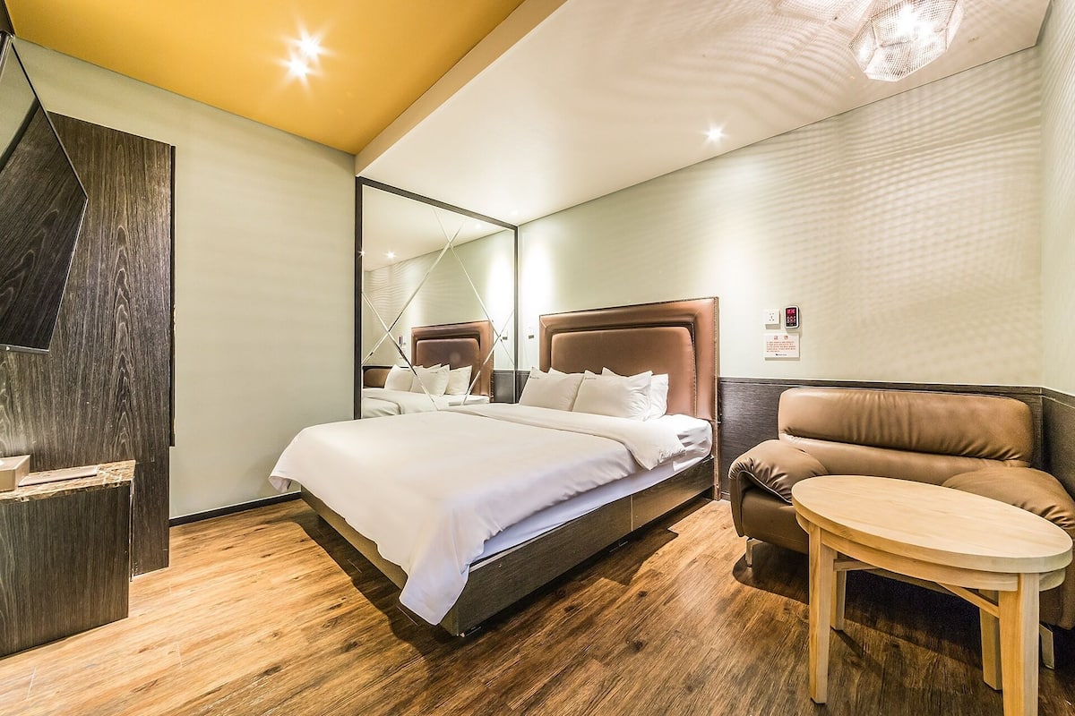 Una habitación de hotel moderna con una cama grande, una zona de estar y un espejo.