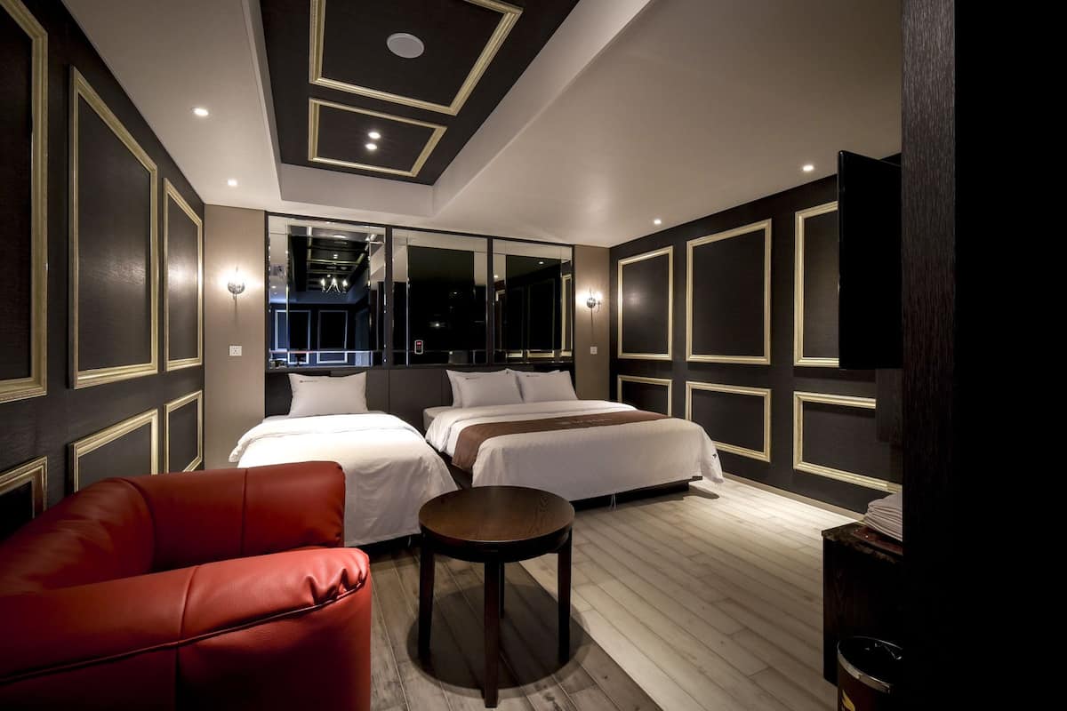Habitación de hotel con dos camas, una silla roja, una mesita redonda y un televisor en la pared.