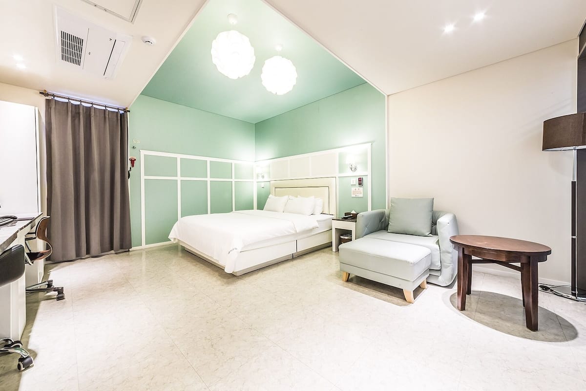 Una habitación de hotel con cama, escritorio con silla, una mesita y un sofá.