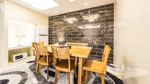 Un comedor con mesa y sillas de madera, microondas y pared de baldosas oscuras.