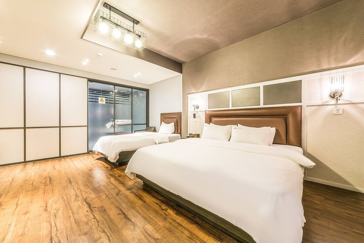 Habitación de hotel con dos camas, piso de madera, un ventanal grande y una lámpara moderna.