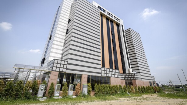 Un moderno edificio de hotel con un llamativo letrero que dice 'Hotel Arisu', que presenta una fachada única a rayas y una entrada amplia con una marquesina de vidrio.