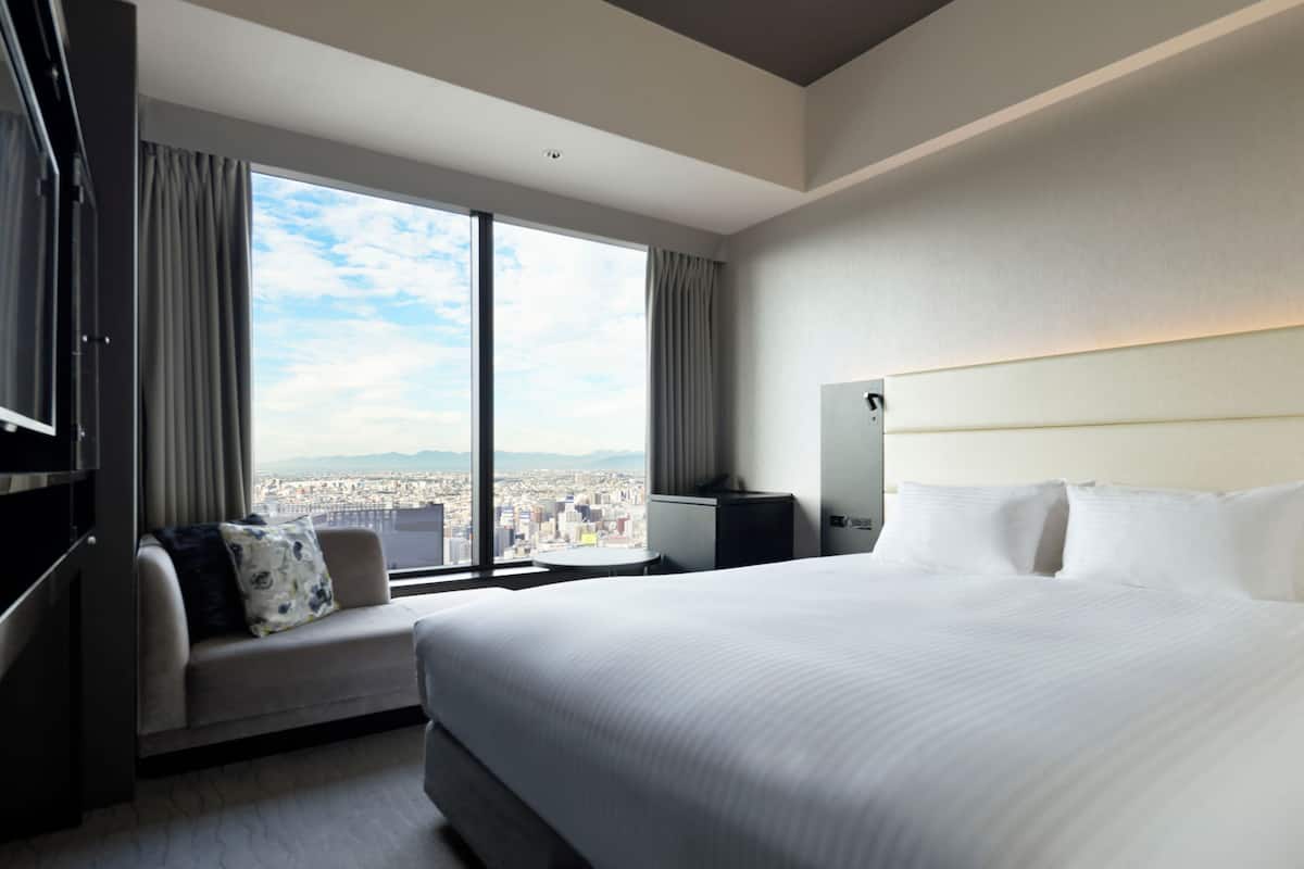 Une chambre d’hôtel avec un grand lit, un canapé, une télévision et une vue sur la ville.