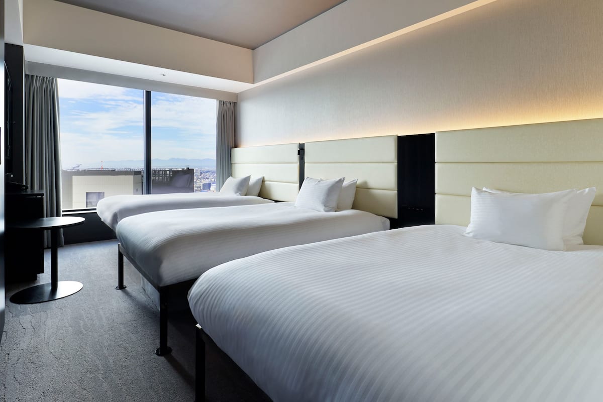 Une chambre d’hôtel avec deux lits, un bureau et une grande fenêtre donnant sur la ville.