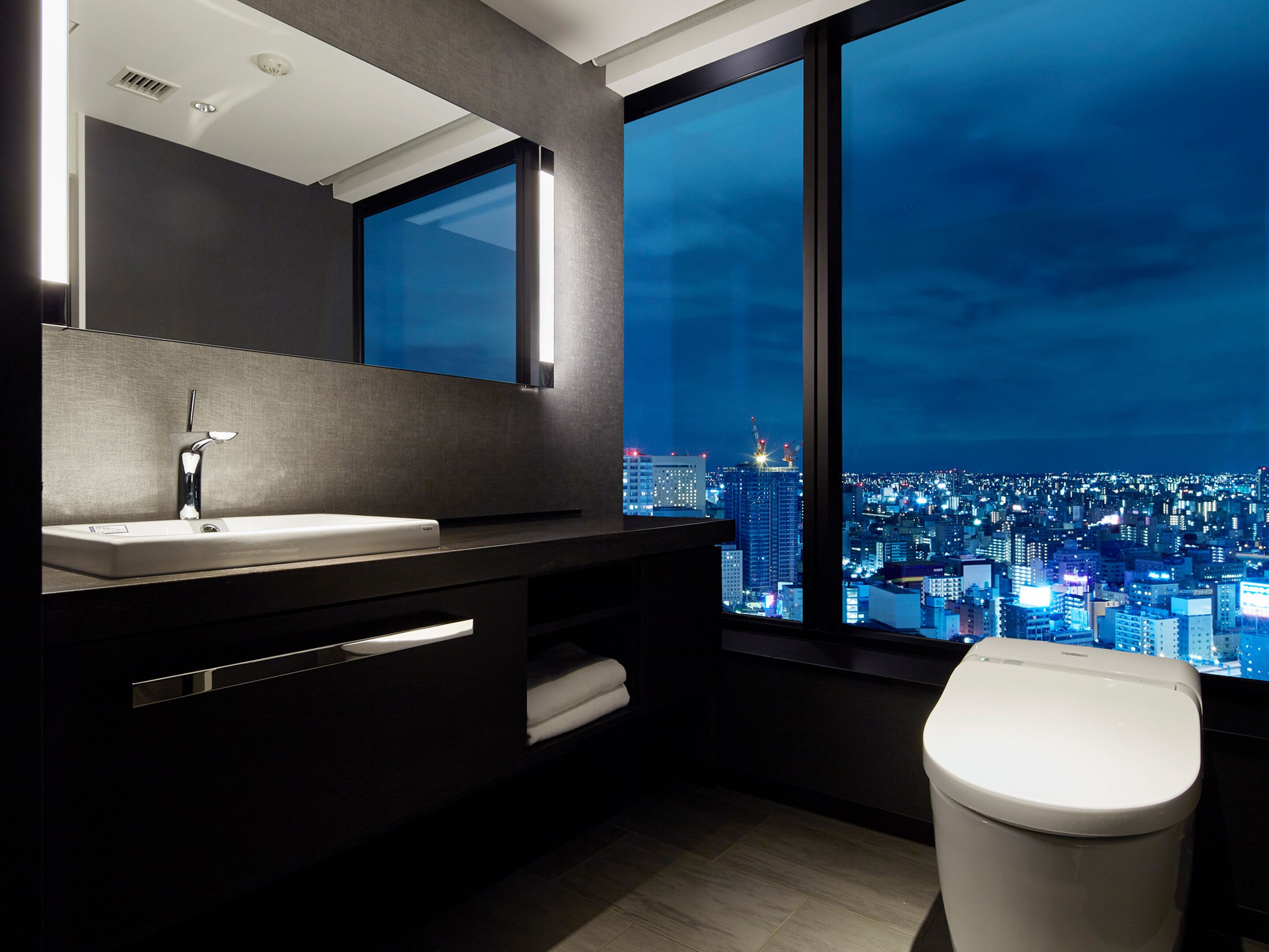 A modern bathroom with a large window, a sink, and a toilet.