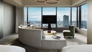 A modern hotel room with a curved sofa, a flat-screen TV, and a city view.