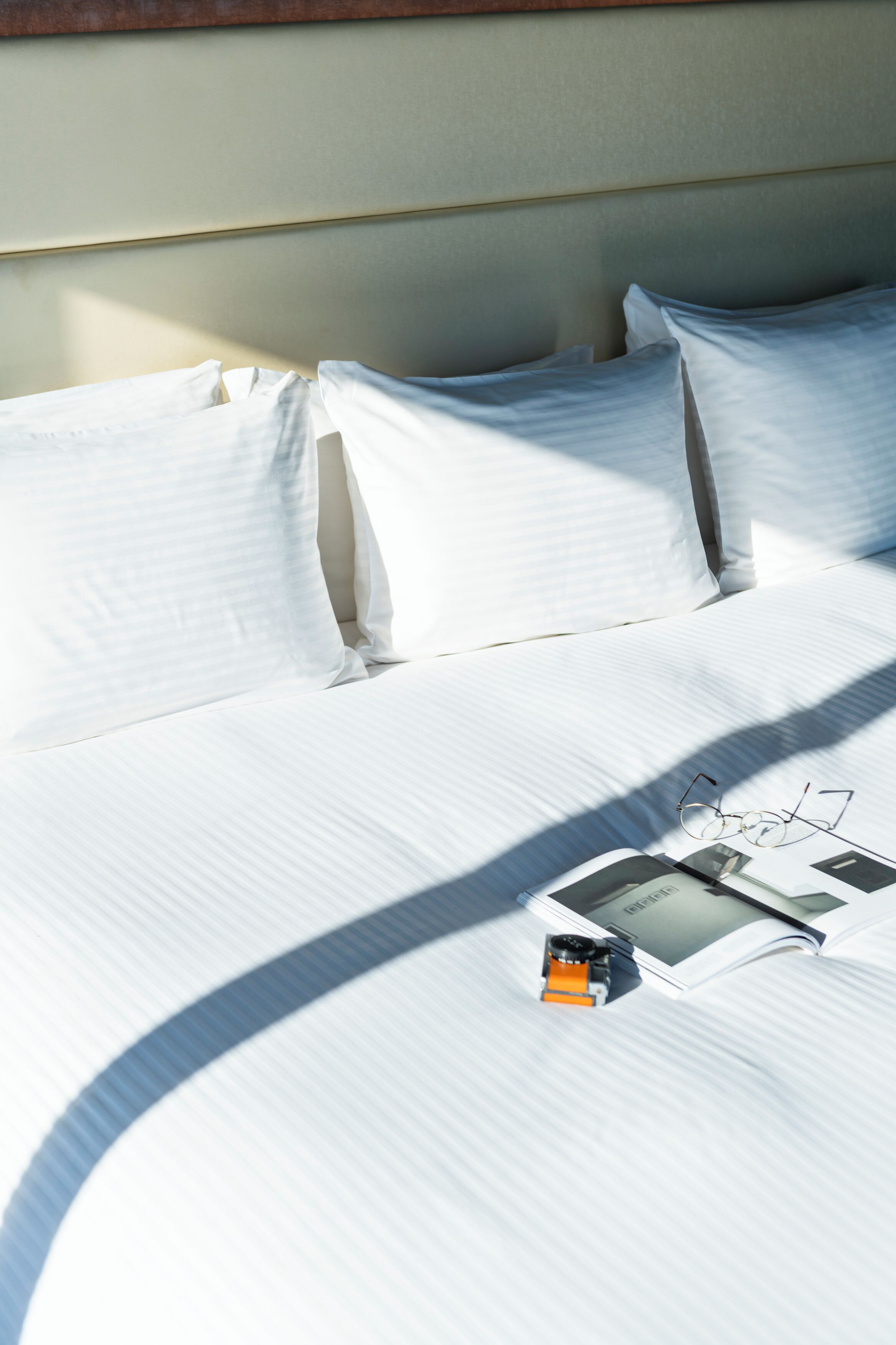 A neatly made bed with white linens, a pair of glasses, and a book on the bed.