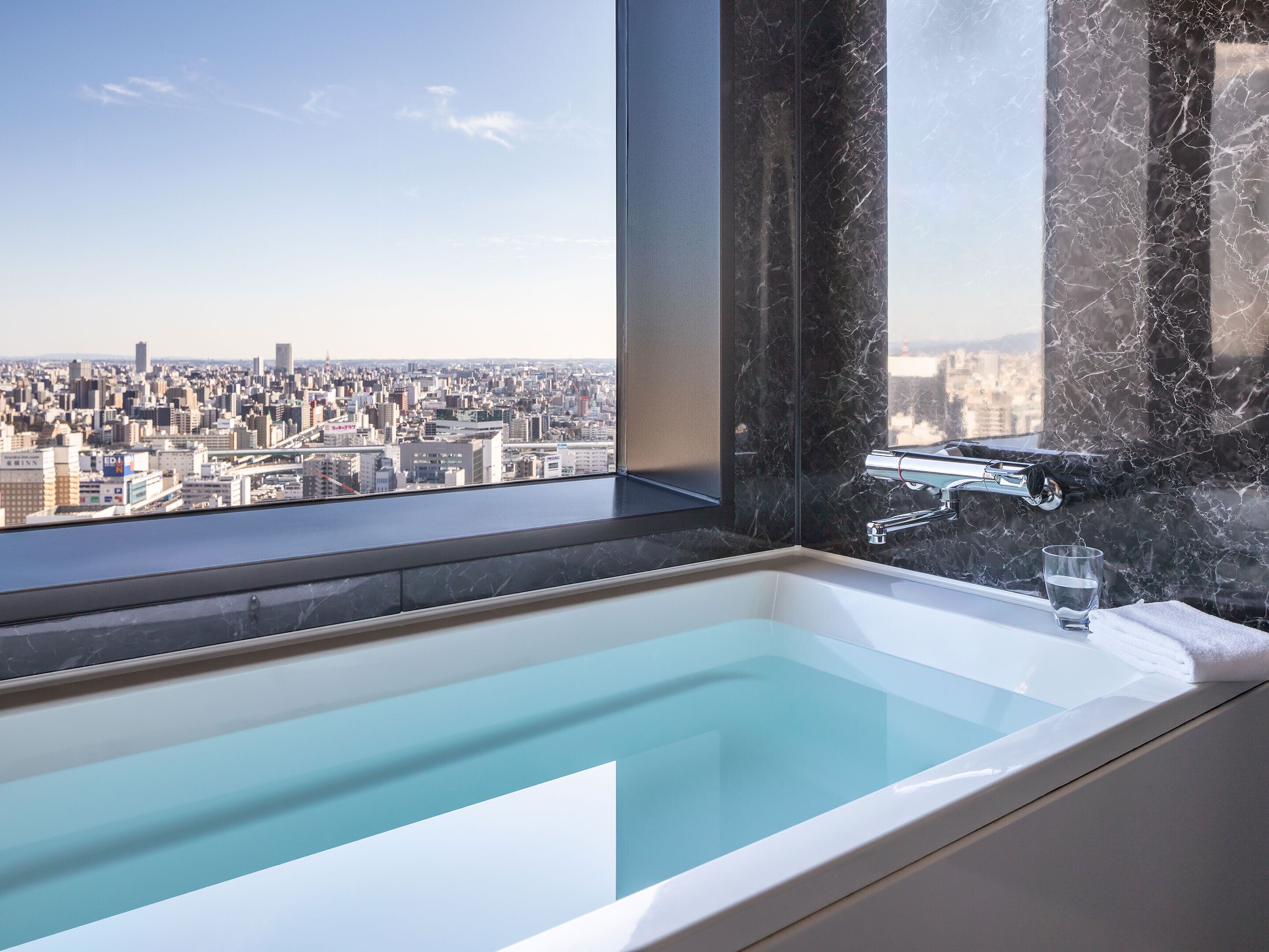 A modern bathroom with a large bathtub, a glass of water, and a city view.