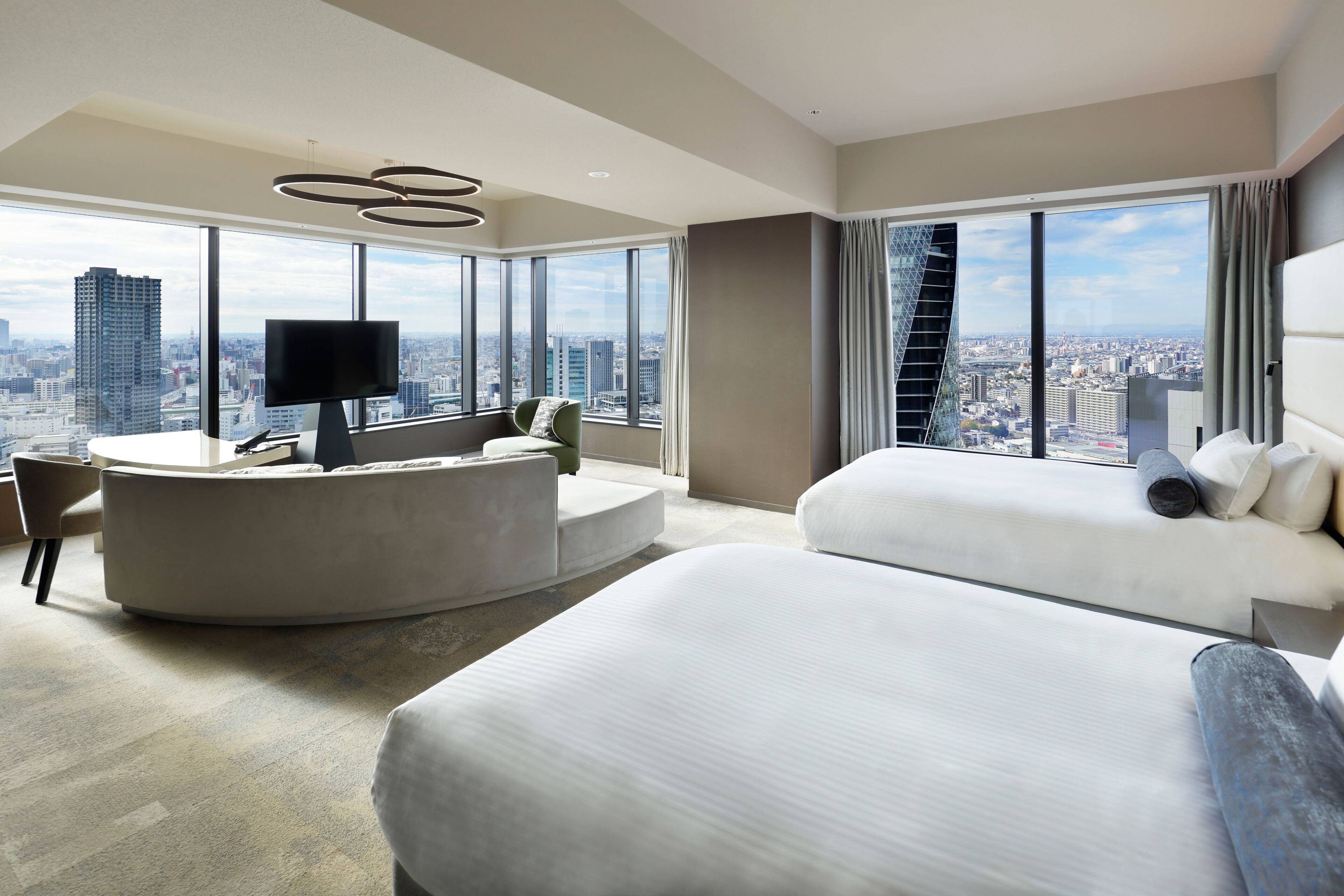 A modern hotel room with a curved seating area, a large bed, and a city view.