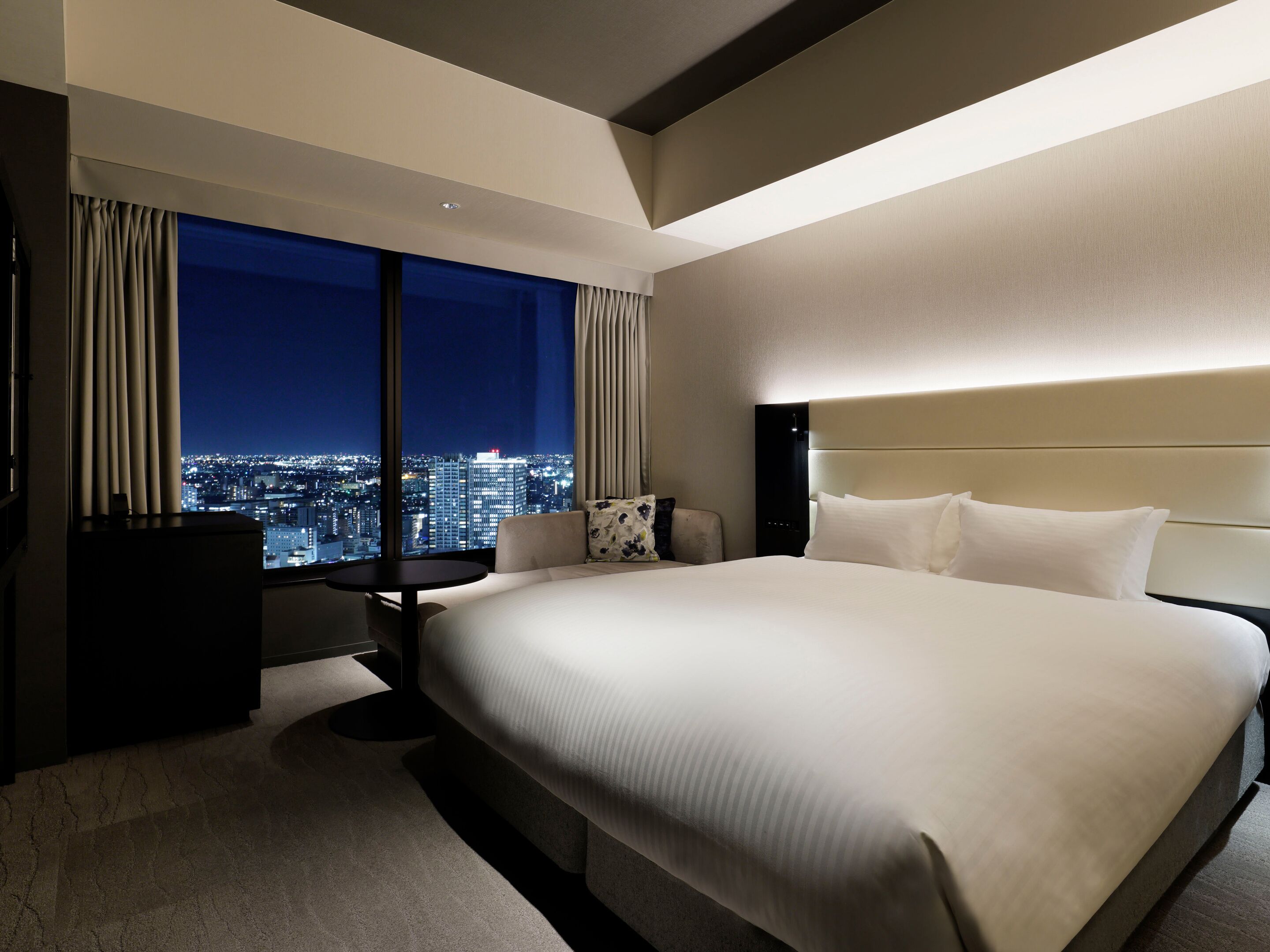 A hotel room with a large bed, a desk, and a view of the cityscape.