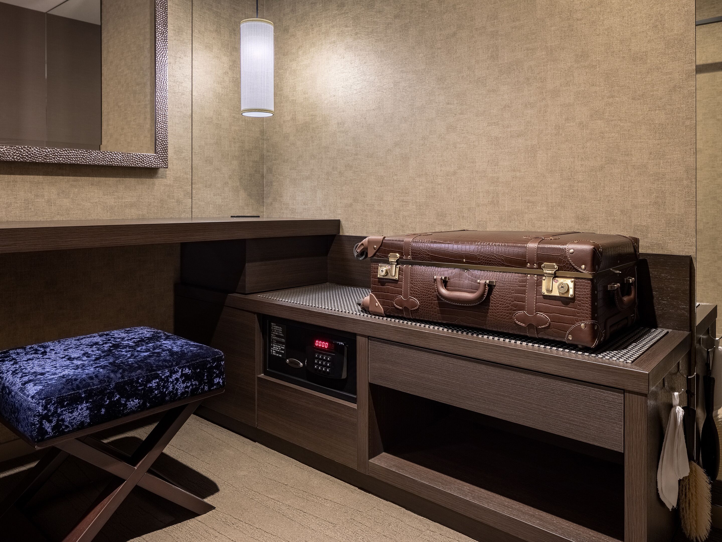 A compact room with a wooden bench, a suitcase, a digital clock, and a mirror on the wall.