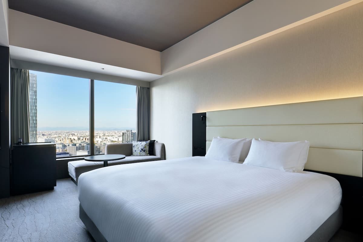 Une chambre d’hôtel avec un grand lit, un canapé, une petite table et une vue sur la ville.