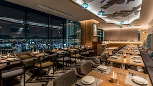 Un restaurante moderno con vistas a la ciudad, que cuenta con una mesa común alargada y asientos individuales.