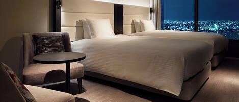 Habitación de hotel con una cama grande, una mesita, una silla y vistas a la ciudad de noche.