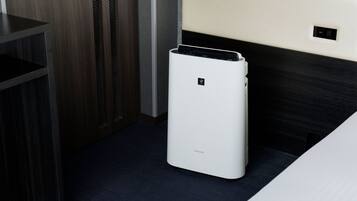 Quarto com ar condicionado branco, piso de madeira escura e vista parcial de uma cama.
